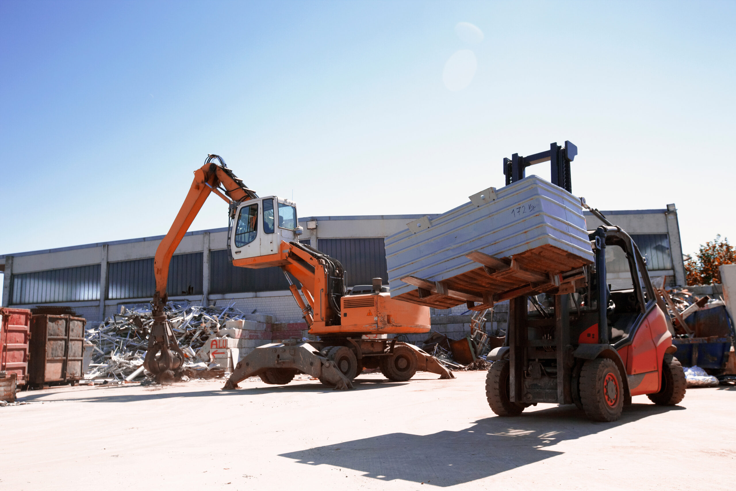 Grue et chariot élévateur triant et déplaçant des métaux dans un parc à ferraille